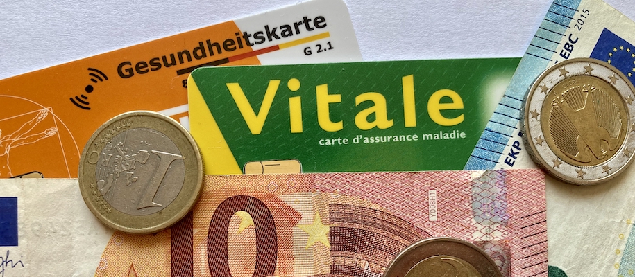 Eine Gesundheitskarte und eine Carte vitale mit Geldscheinen und Münzen bedeckt