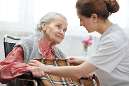 Eine Pflegerin deckt eine ältere Frau im Rollstuhl zu