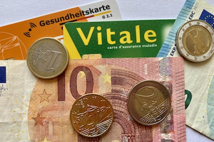 Une "Gesundheitskarte" allemande et une carte vitale couvertes de billets et de pièces de monnaie